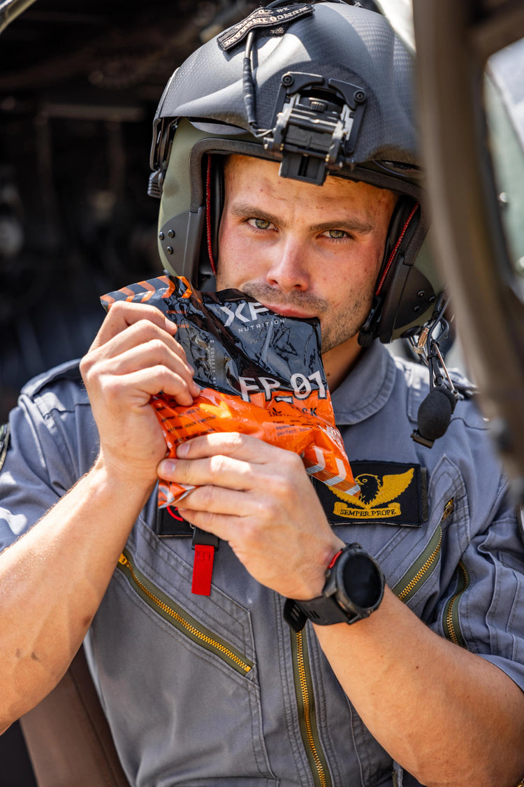 Henco Ingram in a flight suit and helmet holding an XPN Fuel Pack orange bag with a red tag.